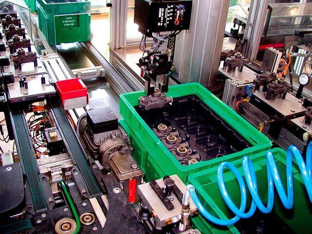 Robot inserts automotive components into slots of thermoformed component holders placed in plastic containers